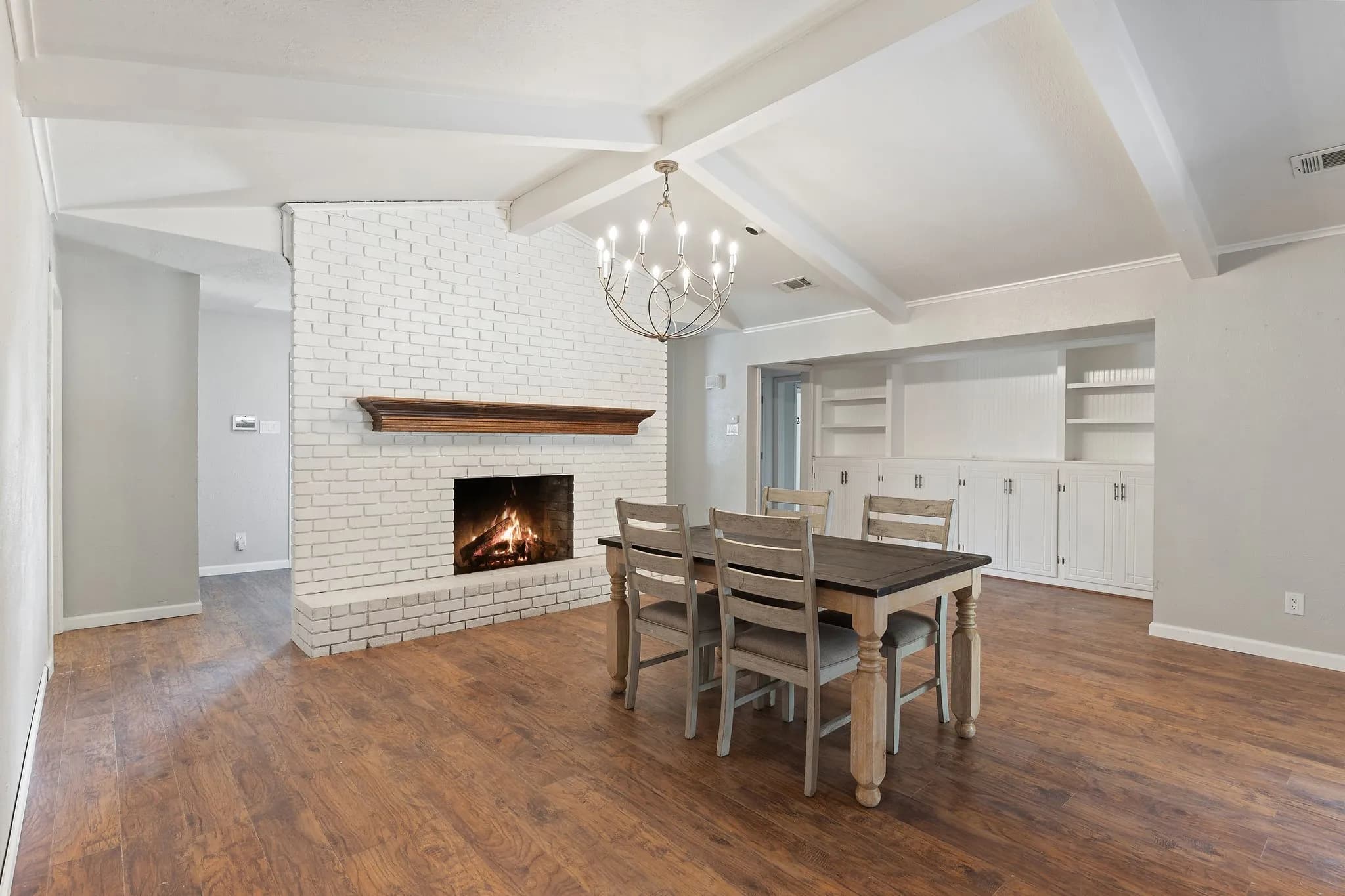 Shared dining area with a wood dining table, a lit brick fireplace, and built-in white shelving